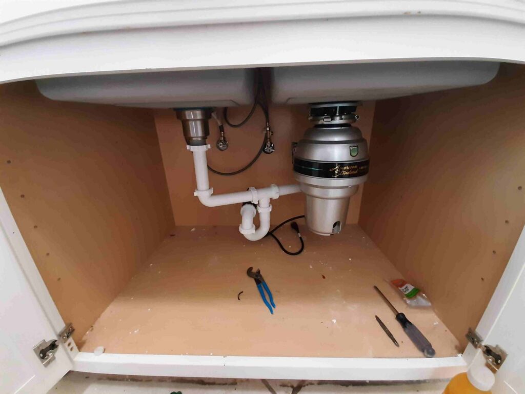 Under a kitchen sink showing new plumbing and garbage disposal installation by Victor White Handyman in Long Beach, CA