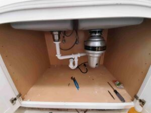 Under a kitchen sink showing new plumbing and garbage disposal installation by Victor White Handyman in Long Beach, CA