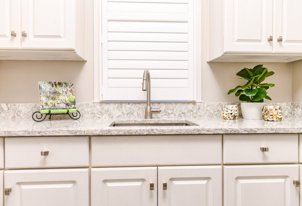 A kitchen sink area with newly installed light granite countertops and white cabinets by Counter Fitters in Savannah, GA