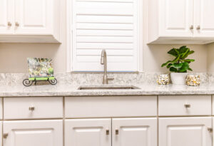 A kitchen sink area with newly installed light granite countertops and white cabinets by Counter Fitters in Savannah, GA