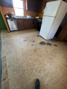 A kitchen with the subfloor exposed and appliances like a refrigerator and dishwasher, indicating renovation prep by Cosa Cleanouts & Junk Removal in Topeka, KS.