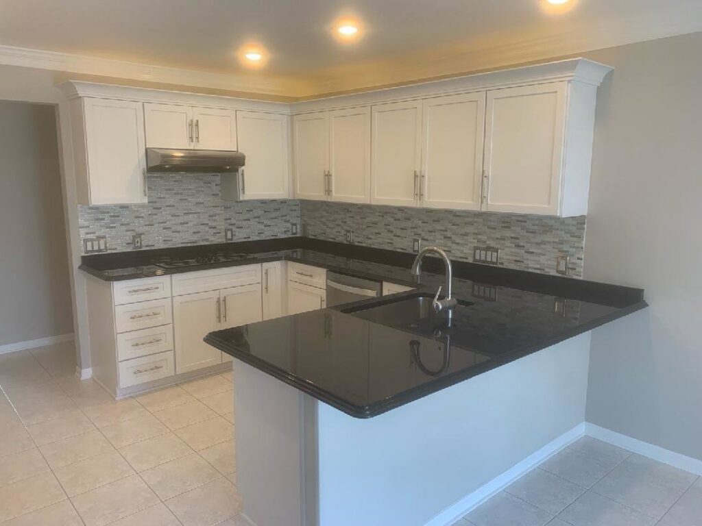 A newly remodeled kitchen featuring white cabinets, black countertops, and a mosaic tile backsplash by Creative Building & Remodeling in Warren, MI