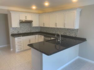 A newly remodeled kitchen featuring white cabinets, black countertops, and a mosaic tile backsplash by Creative Building & Remodeling in Warren, MI