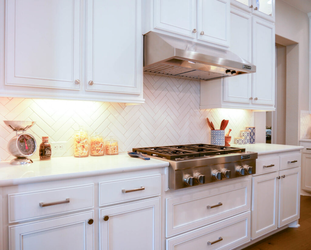 A kitchen remodel showcasing white cabinets, white countertops, and a stylish herringbone tile backsplash by AAA Countertops in Austin, TX.