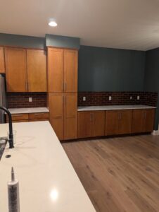 A renovated kitchen featuring wooden cabinets, white countertops, and a stylish dark green accent wall by RAW Renovation in Denver, CO.