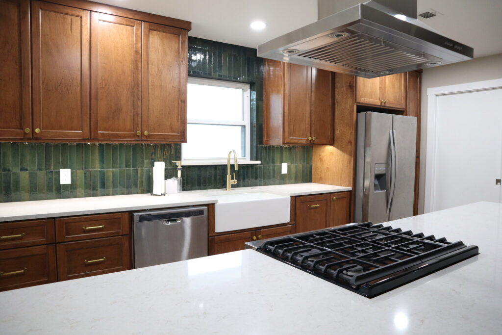 A renovated kitchen with warm wooden cabinets, a vibrant green tiled backsplash, and a farmhouse sink by Whole House Remodel & Design North Dallas Tx in Frisco, TX.