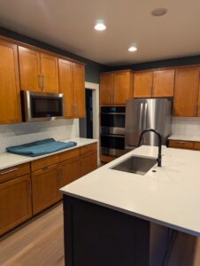 A renovated kitchen with warm wooden cabinets, white countertops, and stainless steel appliances by RAW Renovation in Denver, CO.