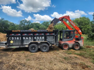 A Kubota skid-steer loader dumping wood chips into a Waste Warrior junk removal trailer in Wichita, KS.
