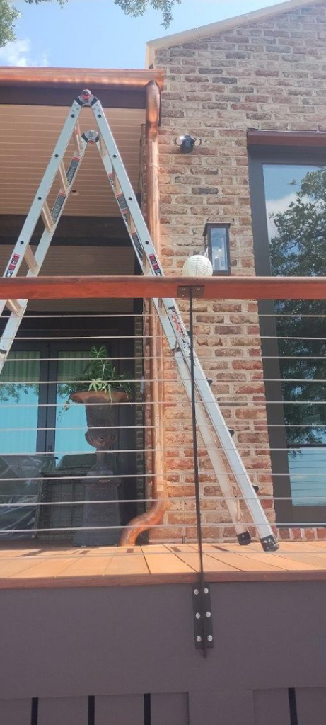 A ladder leaning against a brick house with newly installed copper gutters by Charleston Exteriors in Charleston, SC.