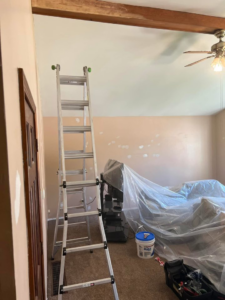 A ladder and covered furniture in a room, indicating preparation for painting or repair work by Honest Help in Fort Wayne, IN