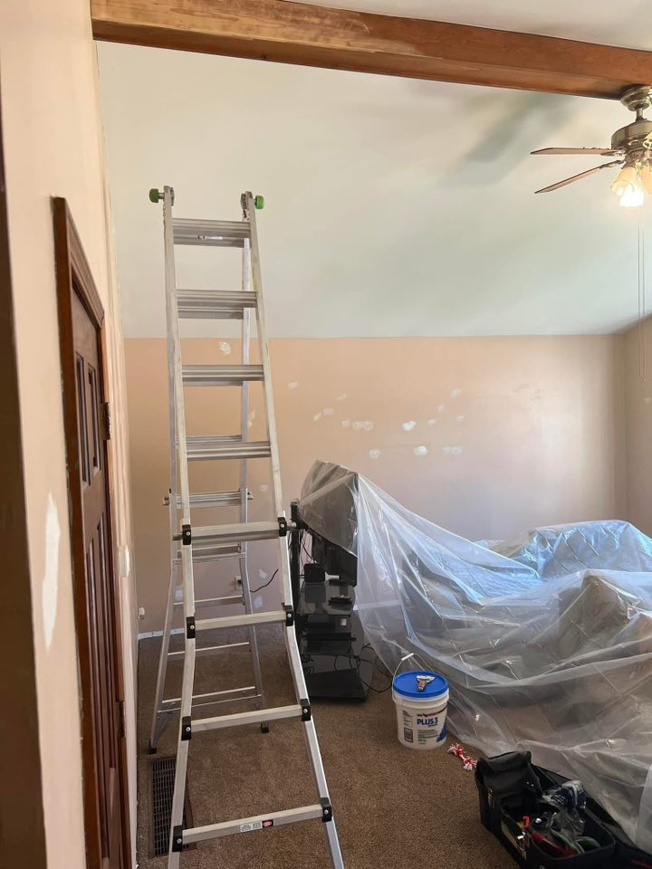 A ladder and covered furniture in a room, indicating preparation for painting or repair work by Honest Help in Fort Wayne, IN