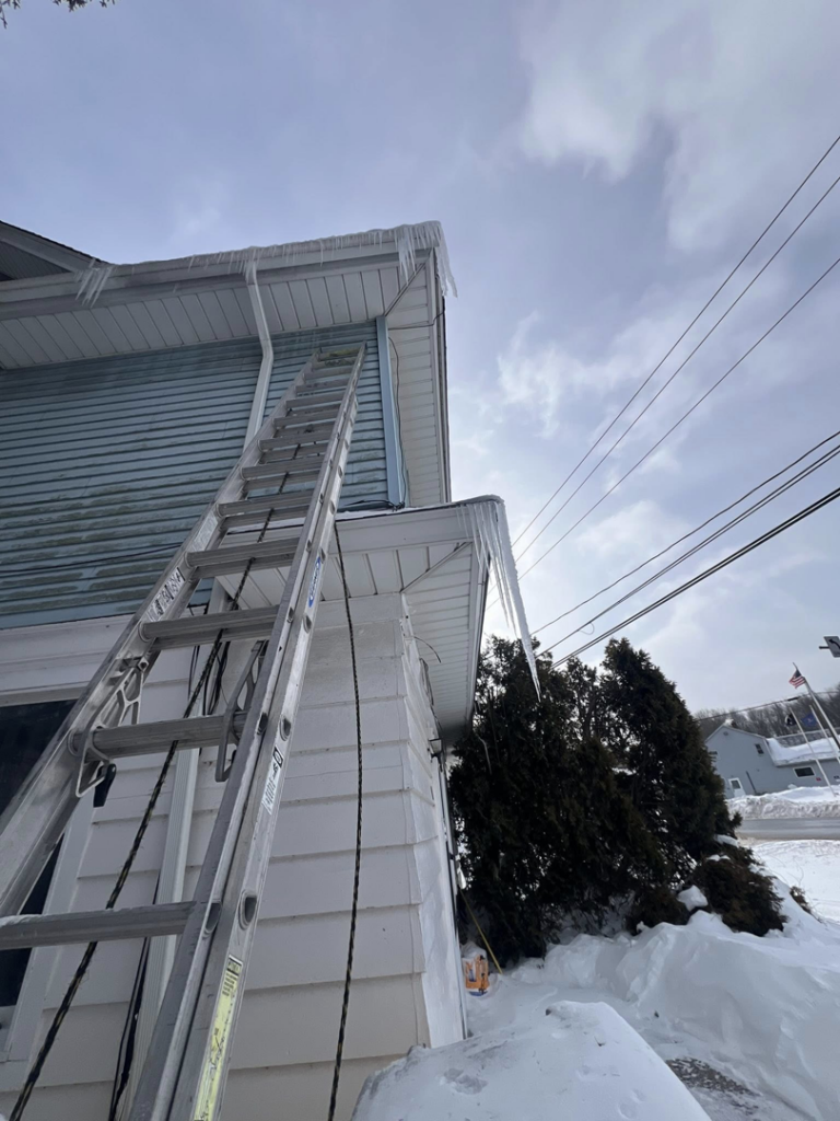 A ladder positioned for gutter or roof repair, with icicles hanging from the eaves, by Manny General Construction Llc in Scranton, PA.