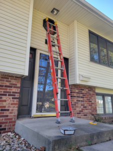 A tall ladder leaning against a house under an outdoor light fixture, set up for repair or replacement by Cedar Valley Maintenance and Handyman Services LLC in Waterloo, IA.