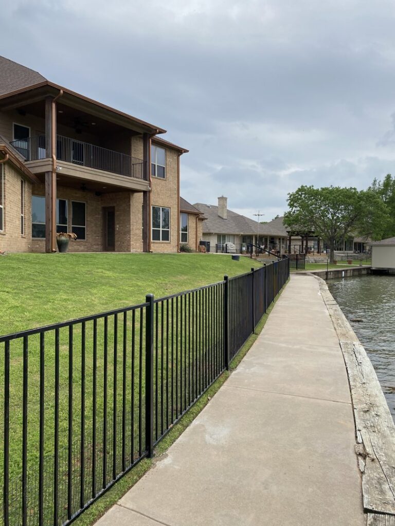 A lakefront property featuring a newly installed black metal fence and concrete walkway by Falls Contracting, LLC in Raleigh, NC.