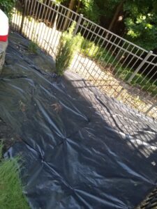 Landscape fabric being installed along a fence line by Mels Haul & Junk Removal in Raleigh, NC.