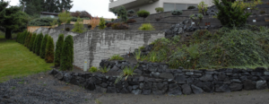 A beautifully landscaped hillside with stone retaining walls and evergreen trees by M.C.Dirtworks in Caldwell, ID.