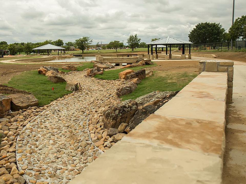 A newly landscaped park area with a dry creek bed and stone walls, completed by Northstar Construction, LLC in Fort Worth, TX