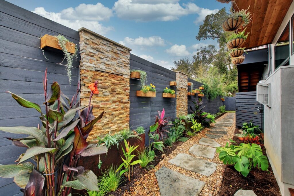 A beautifully landscaped pathway featuring stone pavers, gravel, and a wooden fence with integrated planters by Transformations Custom Build in Austin, TX