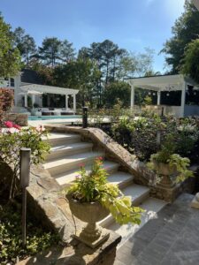 A stone staircase with decorative planters and landscaping leading to a beautiful pool area, a project by Picasso Poolscapes in Johns Creek, GA.