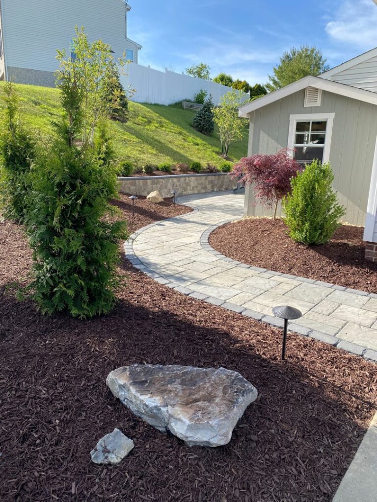 A beautifully landscaped area featuring a paved walkway, retaining wall, and a small shed by JDM Outdoors of Robinson in Pittsburgh, PA.