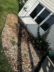 A landscaping bed filled with rocks and dead plants next to a house, showing a scene for yard waste removal by Junk-O-Haulics in Westmoreland, TN.