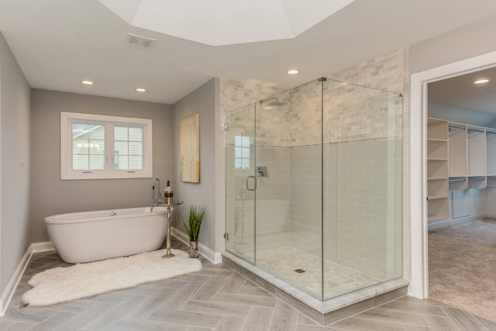 A large, bright bathroom remodel featuring a freestanding tub, glass walk-in shower, and herringbone tile floor by The Bath Shop in Raleigh, NC.