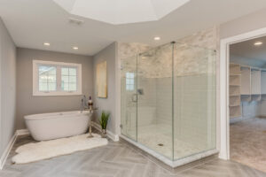 A large, bright bathroom remodel featuring a freestanding tub, glass walk-in shower, and herringbone tile floor by The Bath Shop in Raleigh, NC.