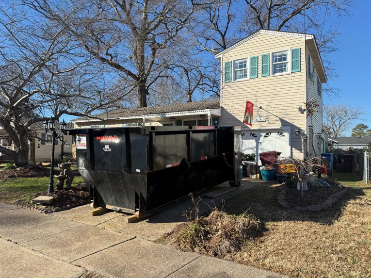 A large black dumpster from Great Bridge Bins, LLC positioned in front of a house for junk removal in Chesapeake, VA.