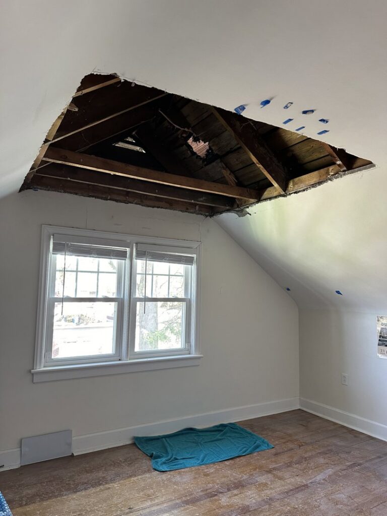 A room with a large hole in the ceiling exposing rafters, indicating a significant repair project by N. Bennecoff Drywall & Plaster in Lancaster, PA.