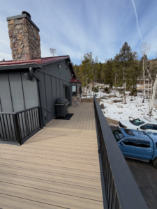 A side view of a house showcasing a large composite deck with black railings and a stone chimney, built by AG - Deck Masters in Arvada, CO.