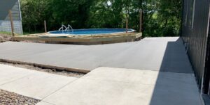 A large concrete patio and walkway leading to an above-ground pool with a wooden deck, installed by Moons Concrete & Construction LLC in Chicago, IL.