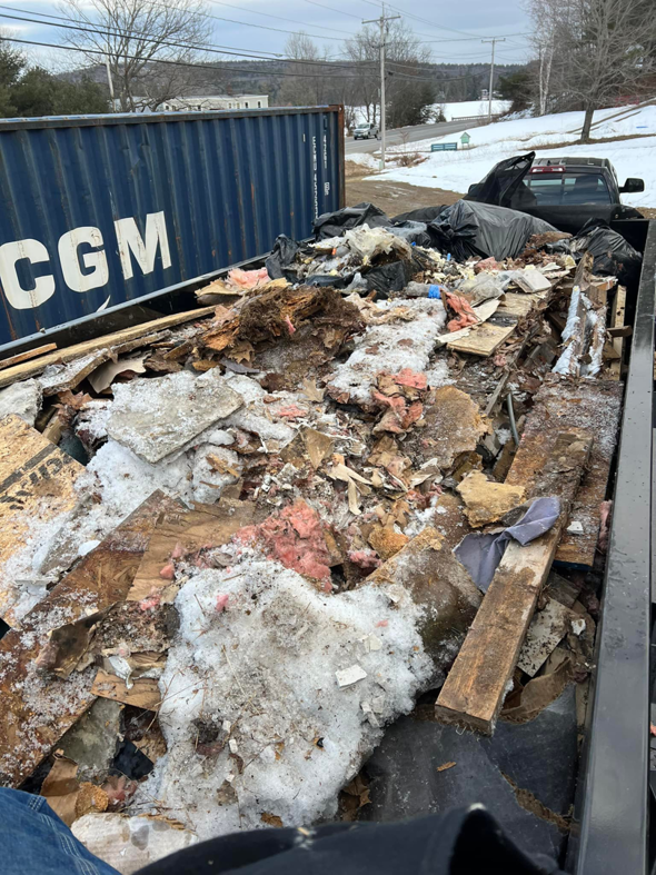 A large container filled with demolition debris, wood, and insulation, partially covered in snow, for removal by Averson Hauling & Disposal LLC in Lebanon, ME