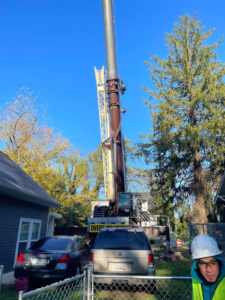 A large crane set up next to a residential home and tall tree for tree removal by Johnson Tree Services in Monrovia, CA.