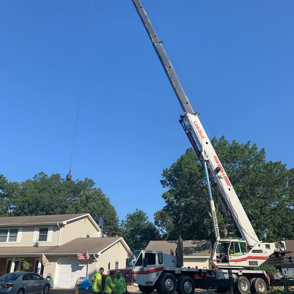 A large crane with an extended boom assisting with tree removal in a residential area for Toms River Tree Service, LLC in Toms River, NJ.