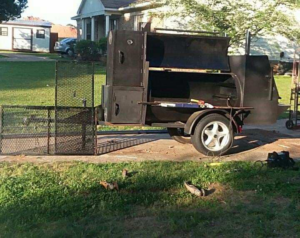 A large custom-built black BBQ smoker on a trailer with multiple compartments open, by Charlotte's Welding Service in Rock Hill, SC