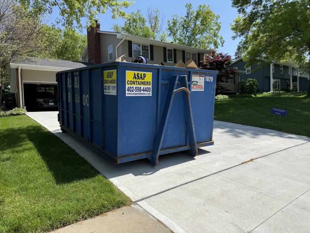 A large blue ASAP Containers inc. dumpster in a residential driveway, ready for junk removal in Omaha, NE.