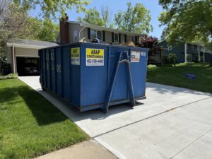 A large blue ASAP Containers inc. dumpster in a residential driveway, ready for junk removal in Omaha, NE.