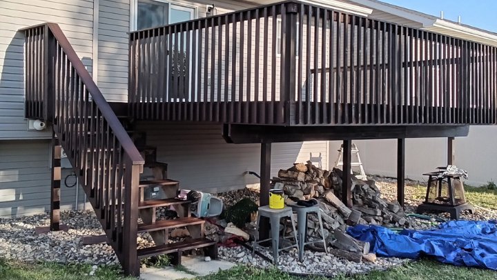 A large elevated wooden deck with dark brown stain and stairs, a completed project by The Creative Carpenter in Minot, ND.