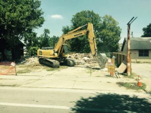 A large excavator working on a demolition site with piles of debris for All Aboard Contractors in Houston, TX.