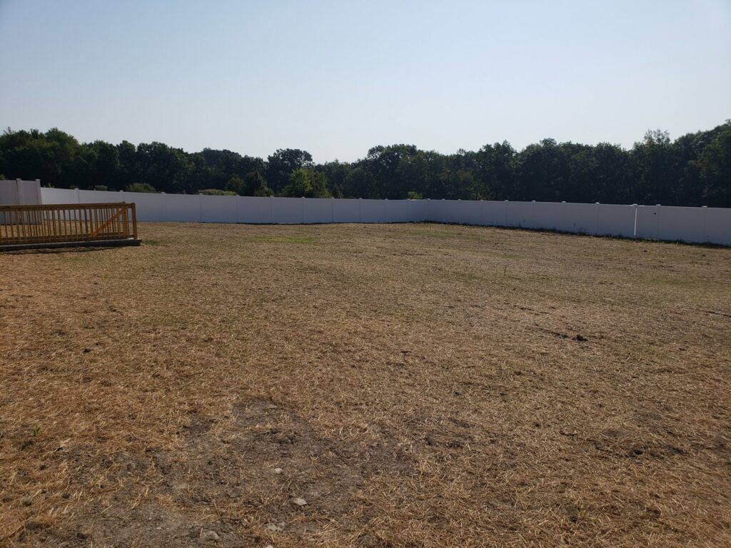 A large field enclosed by a white vinyl fence with a wooden deck, installed by Lee Fence and Outdoor in York, PA.