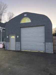 A newly constructed large garage with dark gray siding and a roll-up door by S-Squared Construction in Madison, WI.