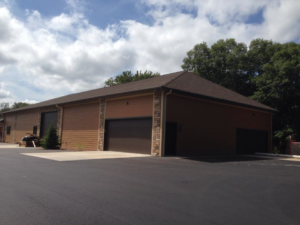 A large, newly constructed garage or outbuilding with stone accents and brown siding by Ankeny Builders L.L.C. in Eau Claire, WI.