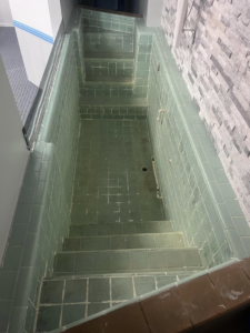 A large, green tiled baptismal pool before professional refinishing by Immaculate Refinishing in Arlington, TX.