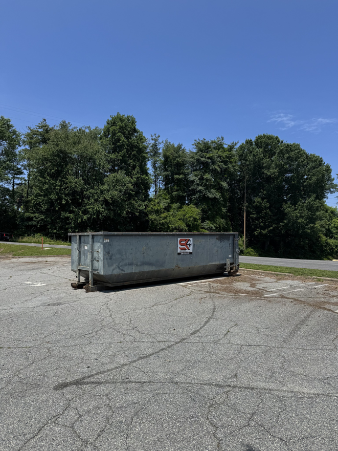 A large grey roll-off dumpster from Stryker Environmental Inc placed in a parking lot for junk removal in Bethel Dr., GA.