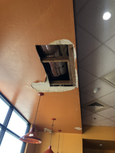 Large irregular hole in an orange ceiling exposing structural elements by Fonseca's Drywall, LLC in Glendale, AZ