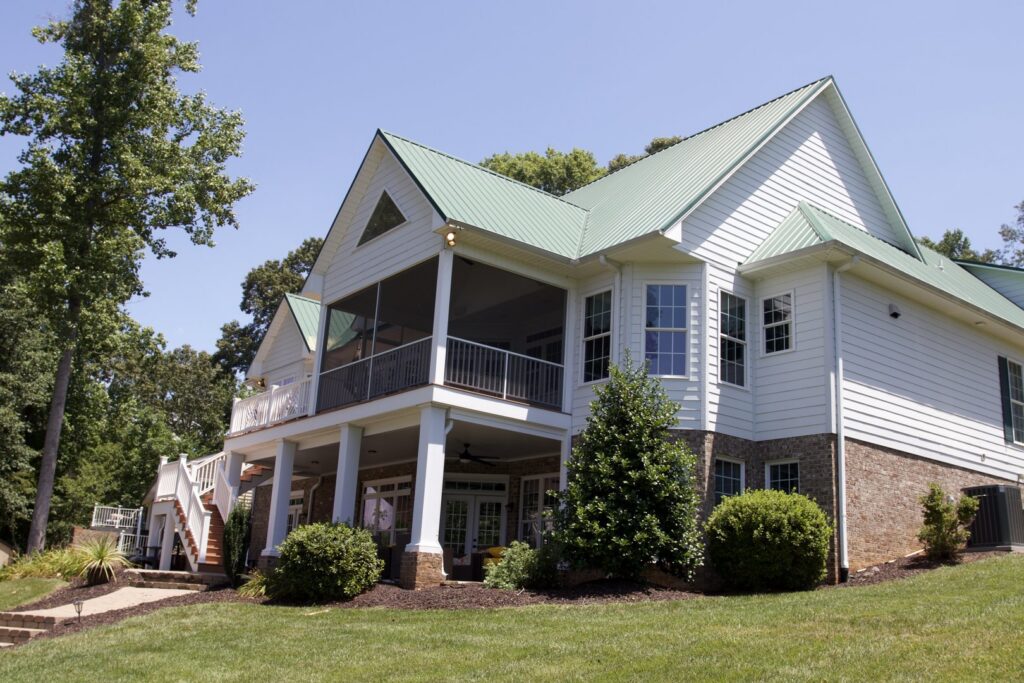 A large house with a newly constructed screened porch and a distinctive green metal roof by Screen Enc in Denver, NC
