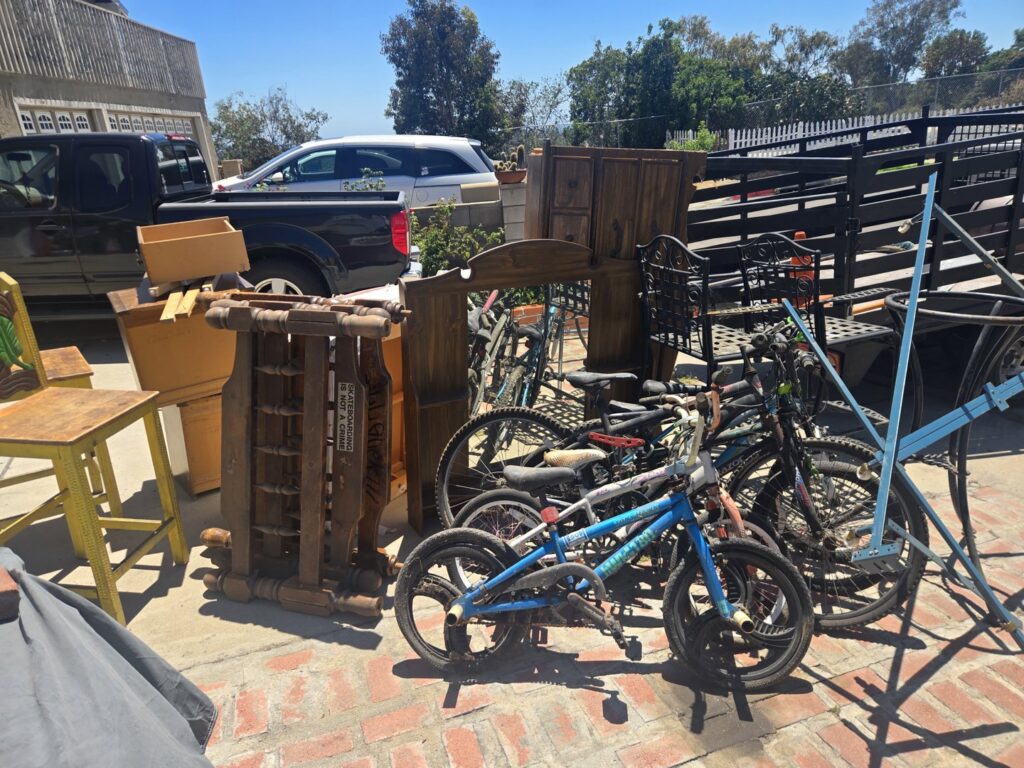 A large pile of junk including bicycles, wooden furniture, and metal items next to a truck for removal by Titan Junk Co. in San Diego, CA