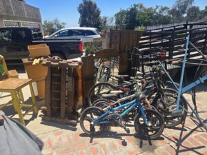 A large pile of junk including bicycles, wooden furniture, and metal items next to a truck for removal by Titan Junk Co. in San Diego, CA