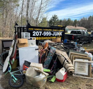 A large pile of various junk ready for removal with a Rubbish Doctor trailer in the background in Portland, ME.