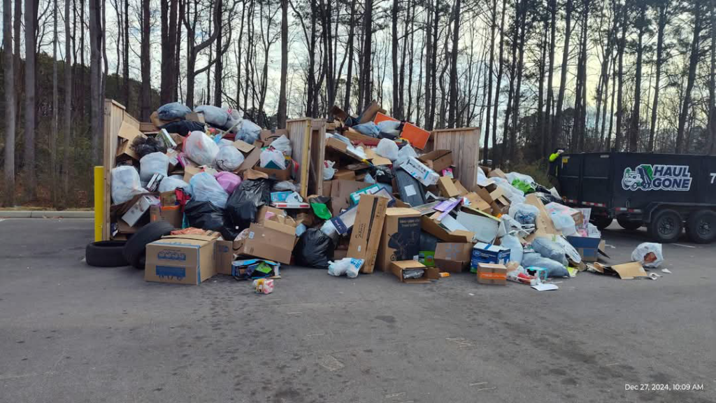A massive pile of residential and commercial junk overflowing from an enclosure, with a Haul Gone 757 trailer in the background, showcasing large-scale junk removal in Chesapeake, VA.